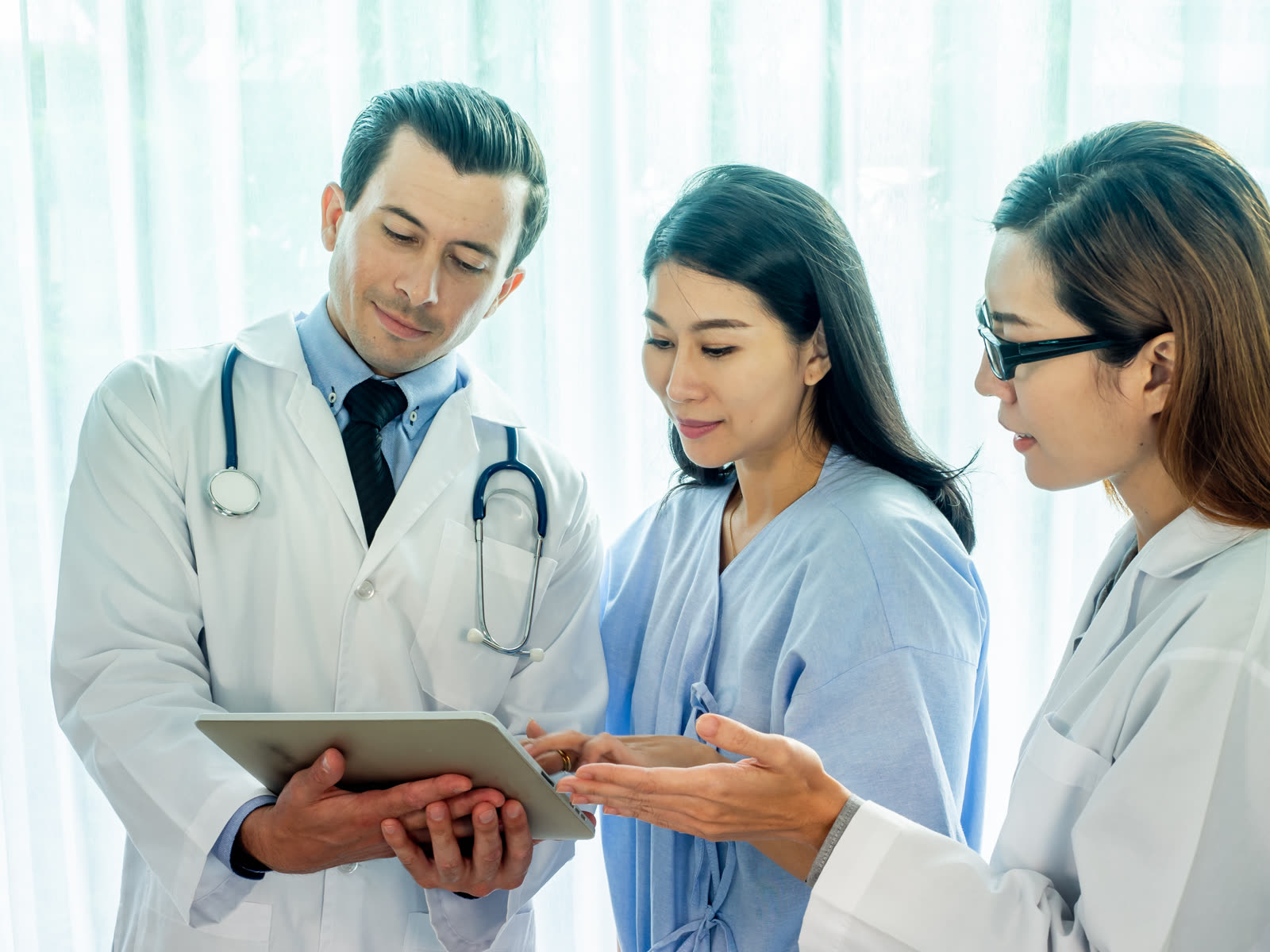 A doctor and a colleague explain test results on a tablet to a patient.
